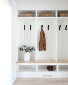 a white coat rack with two coats hanging on it's sides and some shoes next to it