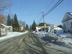 an empty street with snow on the ground and power lines above it in front of houses