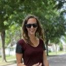 a woman in sunglasses is walking down the street with her hand on her hip and smiling