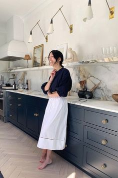 a woman standing in a kitchen next to a counter and shelves with dishes on it