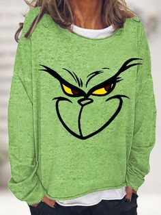 a woman wearing a green sweatshirt with an angry face drawn on the front and yellow eyes