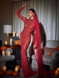 a woman in a red gown and veil posing for the camera with candles around her