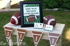 a table topped with footballs and cards on top of a grass covered field next to a sign that says are you ready for some