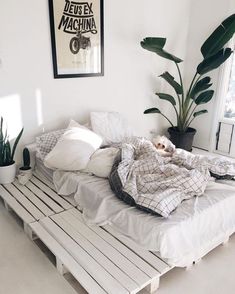 a bed made out of pallets with pillows and blankets on it in a white room