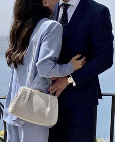 a man and woman kissing each other while standing next to the ocean on a sunny day