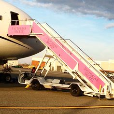 a pink and white jetliner sitting on top of an airport tarmac next to a loading ramp