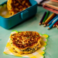 a close up of a sandwich on a napkin near colored pencils and a container