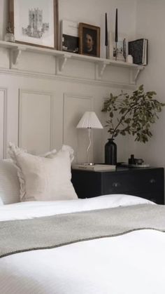 a bed with white sheets and pillows next to a wall mounted shelf filled with pictures