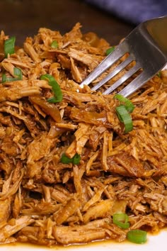 shredded meat on a white plate with a fork in it and garnished with green onions