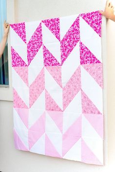 someone holding up a pink and white quilt on the side of a building with windows