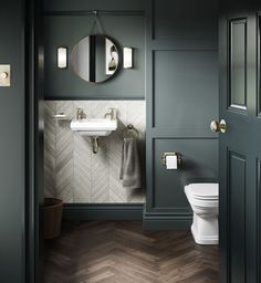 a white toilet sitting next to a bathroom sink under a round mirror on a wall