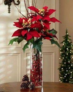 a vase filled with red flowers sitting on top of a table next to a christmas tree