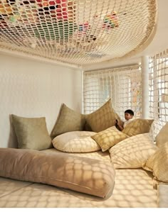 a man sitting on top of a bed covered in pillows next to a net ceiling