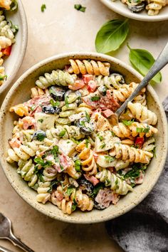 two bowls filled with pasta salad on top of a table next to utensils