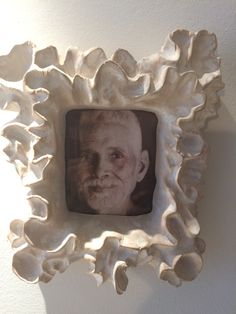 an old man's face is framed in a white shell frame on the wall