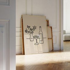 a wine glass and bottle sitting on the floor in front of a framed art piece