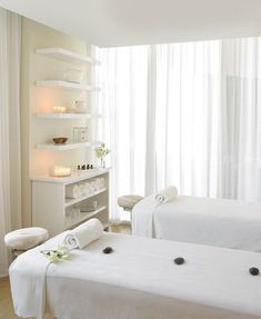 two white beds in a spa room with candles on the wall and towels folded over them