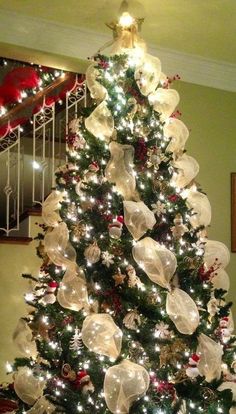 a decorated christmas tree with lots of lights and ornaments on it's branches in front of a staircase