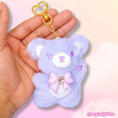 a hand holding a purple teddy bear keychain with a heart on it's chest