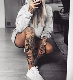 a woman sitting on the floor with tattoos on her arms and legs, holding a cell phone