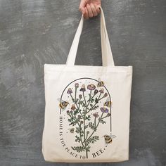 "Add a touch of nature to your everyday style with this charming Wildflower and Bee Canvas Tote Bag. Made from premium textured canvas, this tote features a beautiful print of honey bees and sunflowers. It's perfect for anyone who loves farmers markets or wildflowers. With its gusseted bottom, this tote offers plenty of space for your daily essentials, whether it's books, a planner, or a laptop. It's also great for trips to the farmers market as it can easily hold produce. But the best part? This tote is reusable and eco-friendly, providing a sustainable option for all your shopping needs. * approximately 14\" wide by 15\" tall with a 3\" gusset * printed directly onto the canvas * environmentally friendly print process * 100% heavy poly canvas * 9\" cotton webbed handle * designed and pri Botanical Canvas Bags For Everyday Use, Botanical Style Canvas Bags For Everyday Use, Bag Illustration, Illustration Ideas, Eco Friendly Bags, Textured Canvas, Farmers Markets, Honey Bees, Daily Essentials