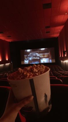 someone holding up a bucket of popcorn in front of a movie screen