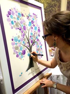 a woman is painting a tree on a canvas