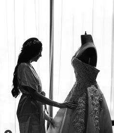 a woman standing next to a dress on a mannequin in front of a window