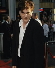 a man in a black suit and white shirt is standing on the red carpet at an event