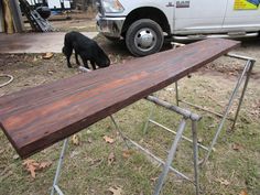 a black dog sniffing at a large wooden object on the ground next to a white truck