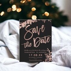 save the date card sitting on top of a bed next to a christmas tree with lights