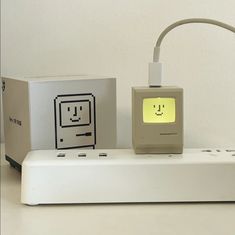 an electronic device with a smiley face on it and two boxes behind it that are also plugged into the charger