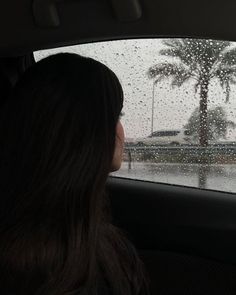 a woman sitting in the back seat of a car on a rain soaked road with palm trees