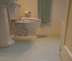 a white toilet sitting in a bathroom next to a sink and bathtub on a tiled floor