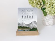 a calendar sitting on top of a wooden stand next to a vase filled with flowers