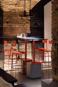 an empty restaurant with orange chairs and barstools in front of a brick wall