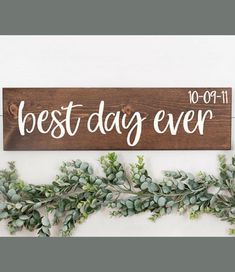 a wooden sign with the words best day ever written on it and greenery hanging next to it