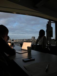 two people sitting at a table with laptops in front of them, looking out the window