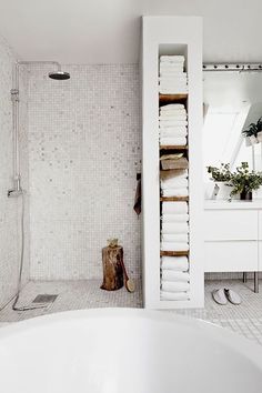 a bathroom with white tiles and towels on the shelf next to the bathtub is shown