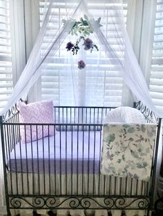 a baby crib in front of a window with white curtains and flowers on it