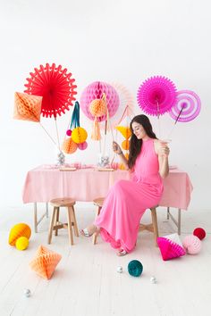 a woman sitting at a table surrounded by paper fans