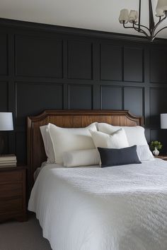 a bedroom with black paneled walls, white bedding and two lamps on either side of the bed