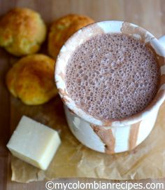 a cup of hot chocolate next to some muffins on a cutting board with butter