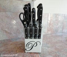 a set of knives in a holder on the floor with marble wall behind it and black handles