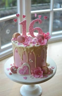 a birthday cake with pink icing and hearts on the top is decorated with flowers