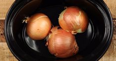 three onions in a black bowl on a wooden table