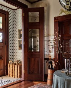 an entryway with wooden doors and baskets on the floor next to it, in front of a wallpapered wall