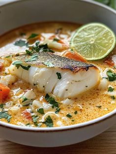 a white bowl filled with fish and vegetables on top of a wooden table next to a slice of lime