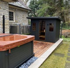 a hot tub sitting on top of a wooden deck next to a stone building with a glass door