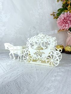 a white paper cut out of a horse drawn carriage with pink flowers in the background